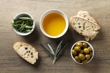 Zeytinyağı, zeytin ve ekmek dilimleri ahşap arka planda, üst manzara