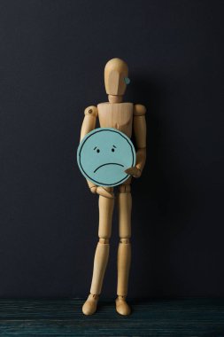 Elinde üzgün emojisi olan tahta adam koyu mavi arka planda.