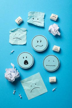 Mavi arka planda hüzünlü emojili kağıtlar, üst görünüm