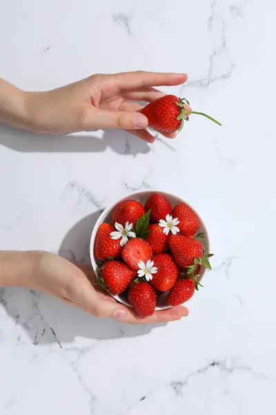 Strawberries in a plate and hands on a marble background, top view