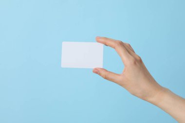 Mavi arka planda, bir kadının elinde beyaz, boş bir kağıt parçası.