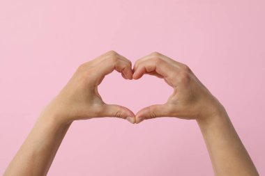 Kadın elleri pembe arka planda parmakları olan bir kalp işareti yapar.