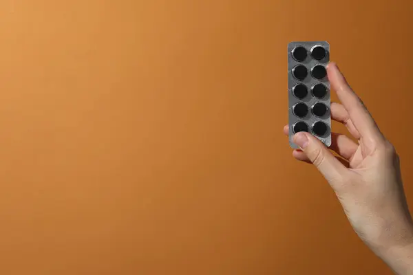 Activated charcoal tablets in hand on orange background