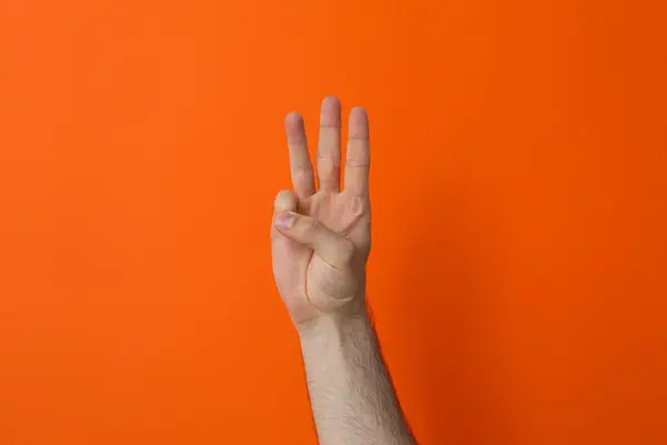 在橙色背景上显示三根手指的女性手 — 图库照片