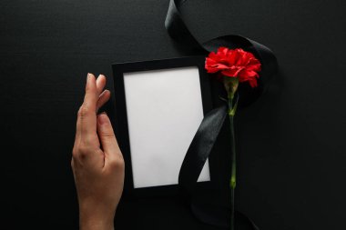 Fotoğraf çerçevesi, çiçek, siyah kurdele ve siyah zemin üzerinde el, üst görünüm