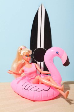 Barbie bebek, sörf tahtası ve mavi arka planda şişme flamingo.