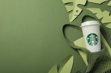Ukrayna, Kyiv, 24 / 08 / 2023: Yeşil arka planda ve çantalı bir fincan Starbucks kahvesi.