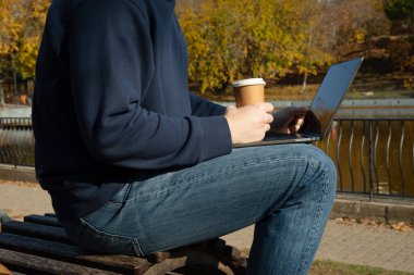 Kağıt bardaklı ve bilgisayarlı bir adam parkta