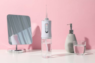 Sulama, ayna ve bir bardak su pembe arka planda.