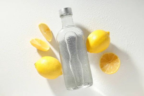 Glass bottle and lemons on white background, top view