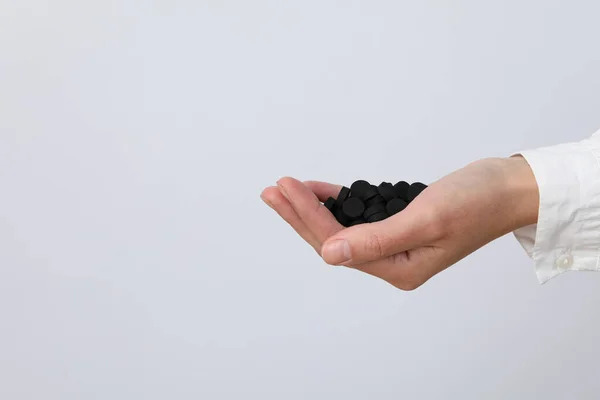Tablets of activated carbon in the hands of a doctor on a light background