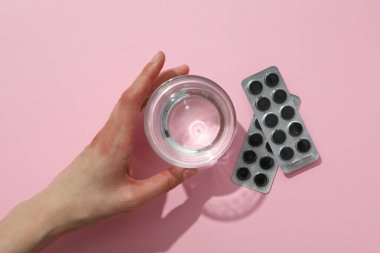 Aktif karbon tabletleri ve pembe arka planda bir bardak su.