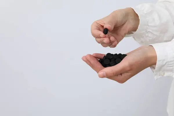 Tablets of activated carbon in the hands of a doctor on a light background