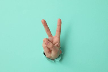 Turkuaz arka planda iki parmağını gösteren bir kadın el.