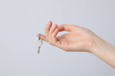 Hafif arka planda, parmağında anahtar olan bir kadın eli.