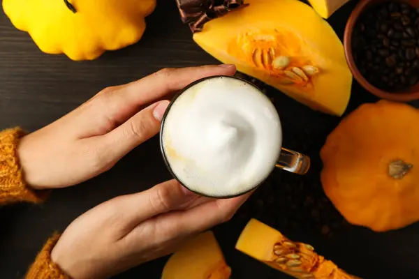 Coffee, pumpkins and female hands on wooden background, top view