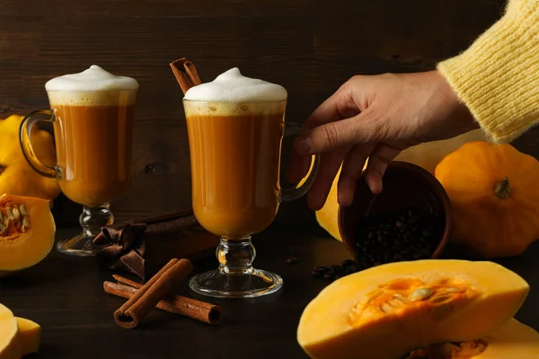 Pumpkin coffee, cinnamon, pumpkins and female hand on wooden background