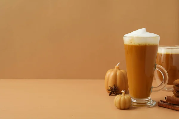 Pumpkin coffee in glasses and candles on brown background, space for text