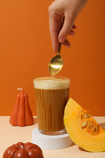 Pumpkin coffee, piece of pumpkin and female hand with spoon on orange background