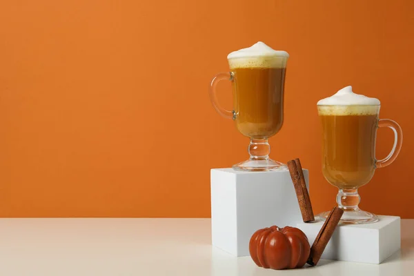 Pumpkin coffee in glasses and cinnamon sticks on orange background, space for text