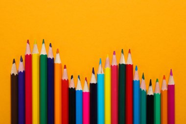 Sarı arka planda renkli tahta kalemler..