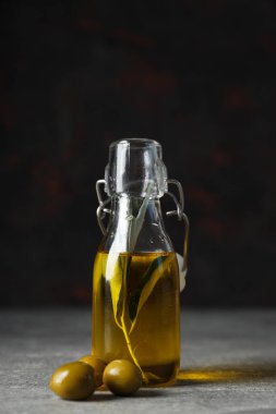 Bir şişe zeytinyağı ve koyu arkaplanda zeytin.