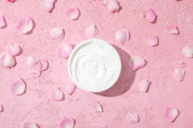 Kremalı kavanoz ve pembe arka planda gül yaprakları, üst manzara.