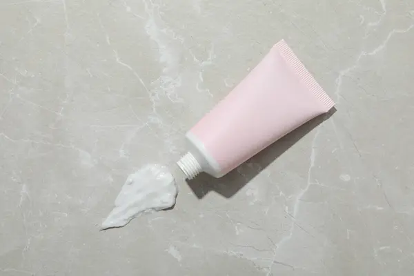 Pink tube with cream on gray background, top view