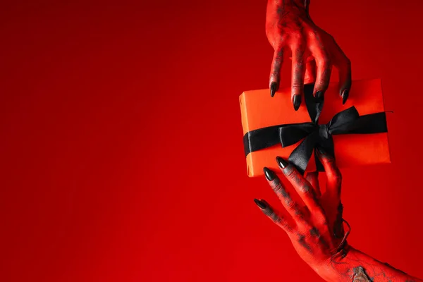 Spooky, red monster hands hold a gift