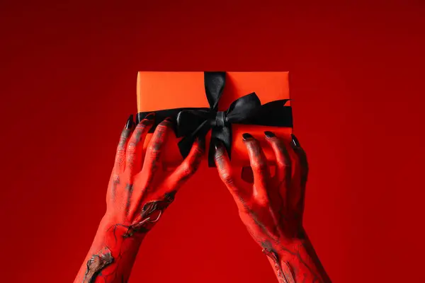 Spooky, red monster hands hold a gift