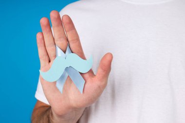 Bir adamın elinde bıyıklı mavi kurdele.