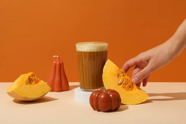 Pumpkin coffee, pumpkins and hand on orange background