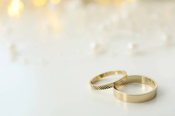 Golden wedding rings on light background, space for text