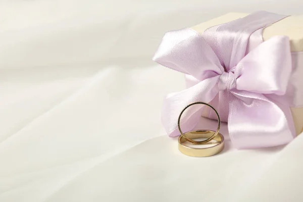 Gift box and wedding rings on light background, space for text