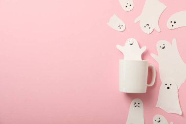 Pembe arkaplanda fincan ve kağıt hayaletler, metin için boşluk
