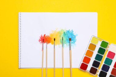Albüm, fırçalar ve boyalar sarı arka planda, üst görünümde