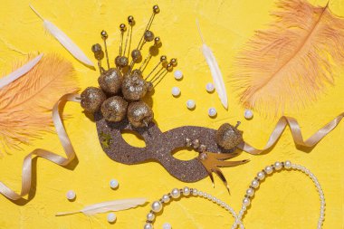 Karnaval maskesi, boncuklar ve tüyler sarı arka planda, üst manzara