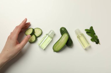 Kozmetik ürünleri, dilimlenmiş salatalık ve beyaz arka planda kadın eli olan şişeler.