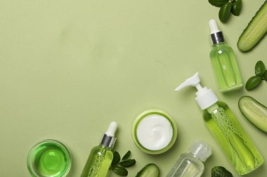 Dilimlenmiş salatalık ve açık yeşil arka planda kozmetik ürünleri olan şişeler, metin için alan