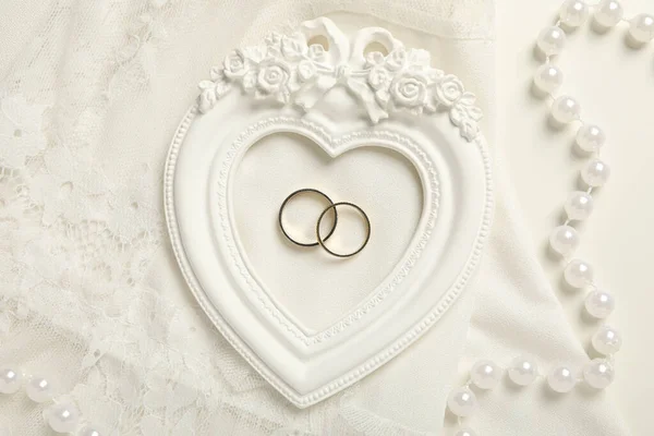 Wedding rings, beads and lace on white background, top view