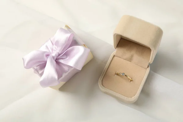 Gift box and wedding ring in case on white background, top view