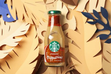 Ukrayna, Kyiv, 24 / 08 / 2023: Muz yapraklarının arka planında Starbucks frappuccino şişesi.