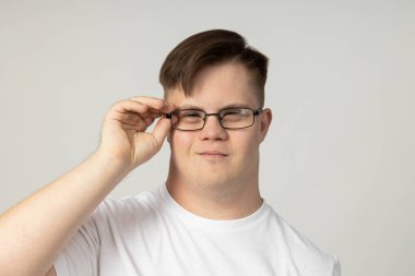 Serebral felçli, gözlüklü ve beyaz tişörtlü gülümseyen genç bir adam kameraya poz veriyor. Dünya Genetik Hastalıklar Günü konsepti