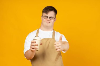 Gözlüklü, kafasında beyin felci olan gülümseyen genç bir adam önlüklü ve kahveli bir barista gibi. Dünya Genetik Hastalıklar Günü konsepti