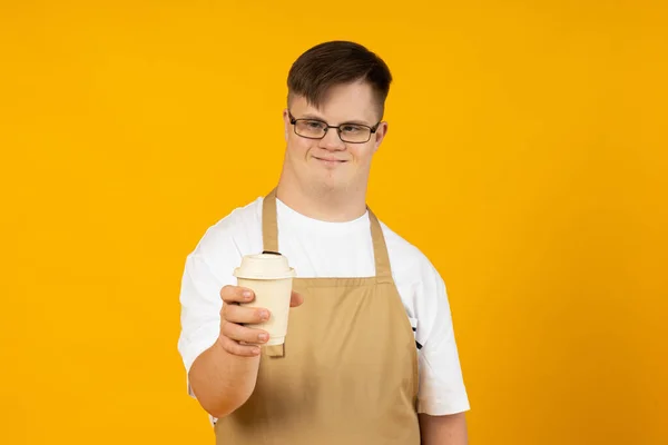 stock image A smiling young man with cerebral palsy in glasses as a barista in an apron and with coffee. World Genetic Diseases Day concept