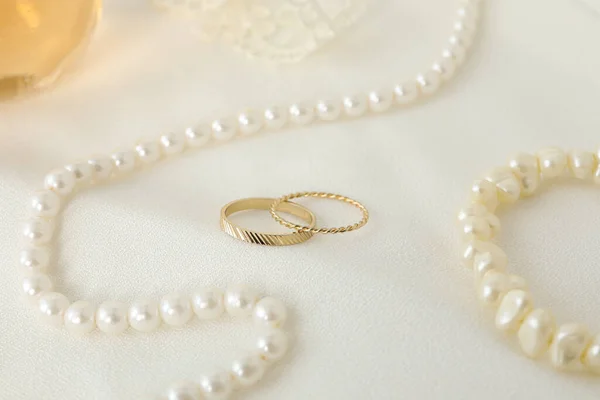 Wedding rings and pearl jewelry on white background, close up