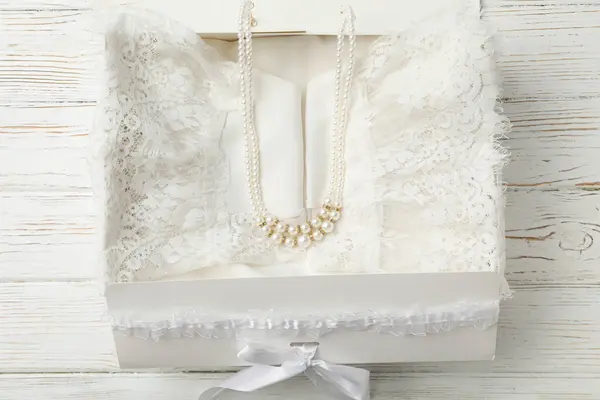 Box with wedding dress and beads on wooden background, top view