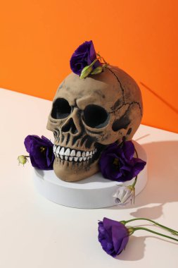 Kafatası ve çiçekler beyaz masada turuncu arka planda