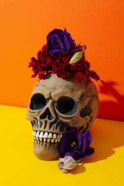 Kafatası ve çiçekler sarı masada turuncu arka planda.