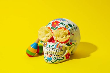 Sarı arka planda Meksika kafatası, çiçekler ve marakas